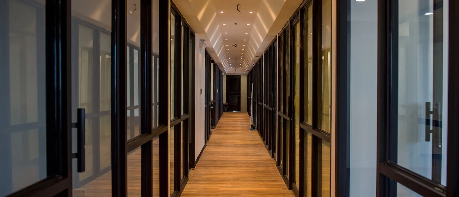 The private office corridor at Acceler8 Rockwell, glass-walled rooms along a wood floor