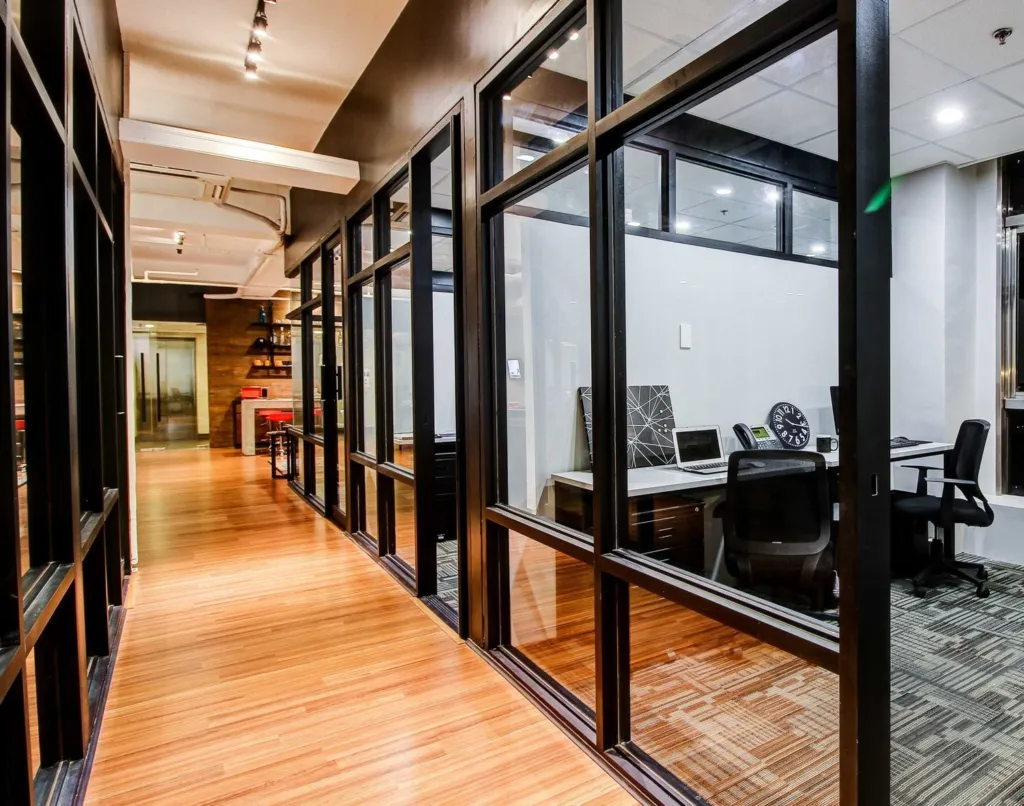 The private serviced office corridor at Acceler8 Salcedo, glass-walled rooms fitted with desks and chairs