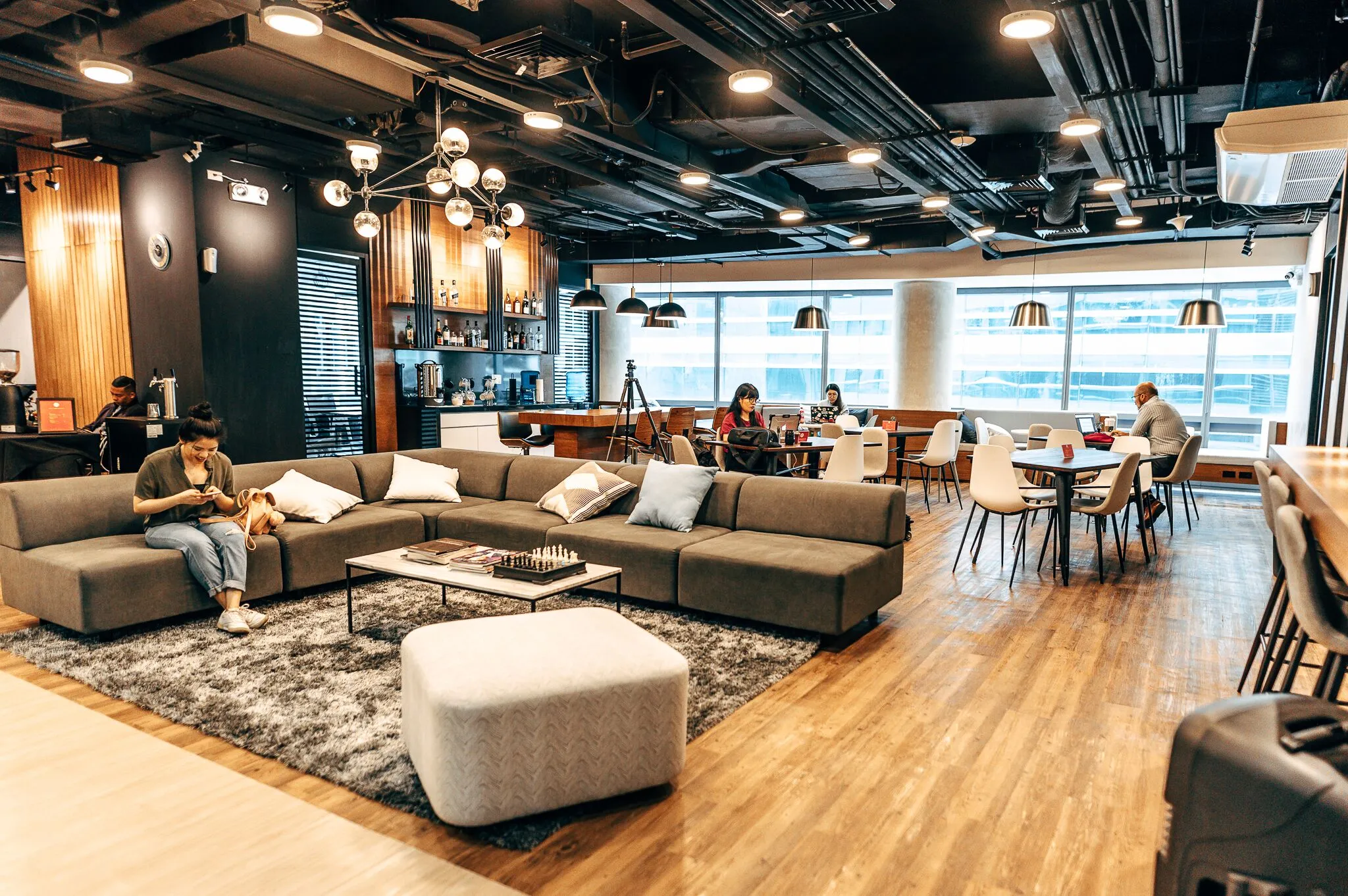 Members working in the Acceler8 Rockwell lounge, with sofas, warm wood floors and city windows