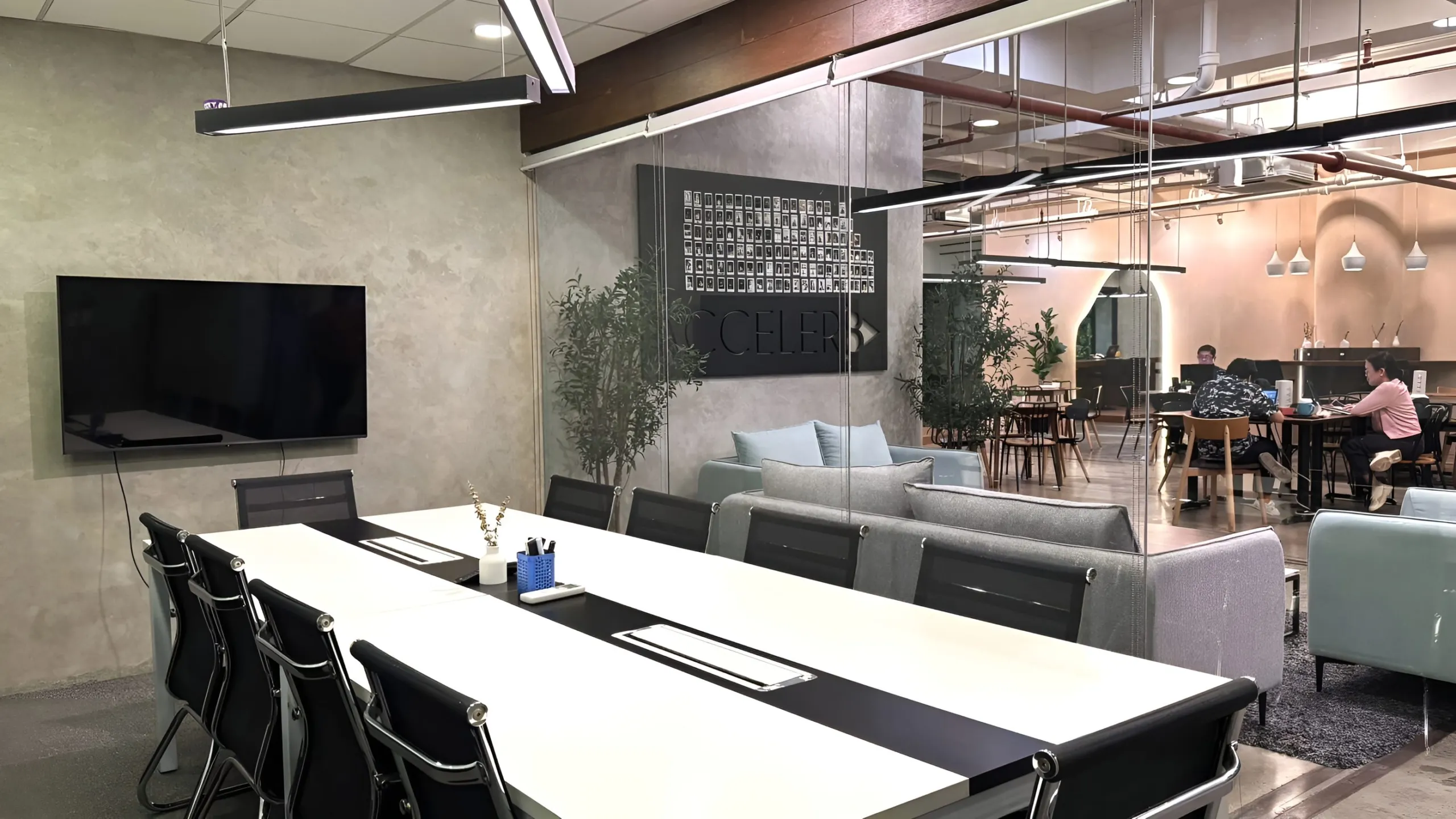 A meeting room at Acceler8 Legazpi with a long table, a wall screen and a view of the coworking lounge
