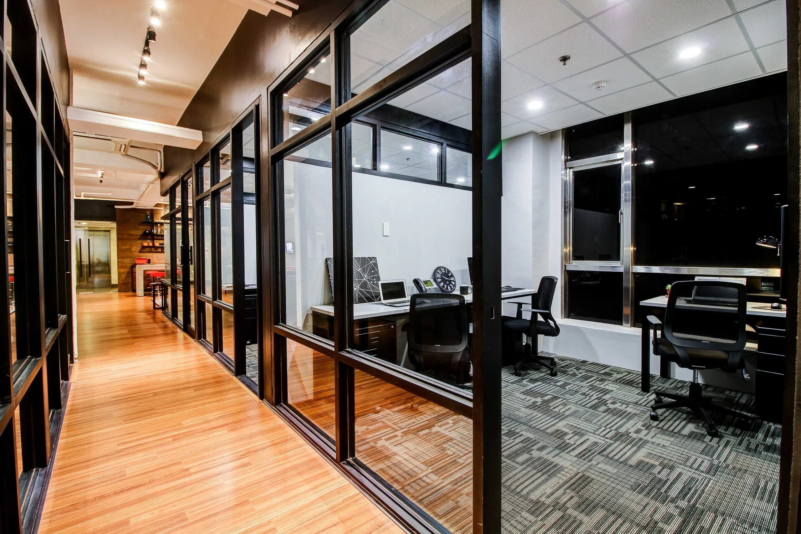 The serviced office hallway at Acceler8 Salcedo, with glass-walled private offices and timber floors